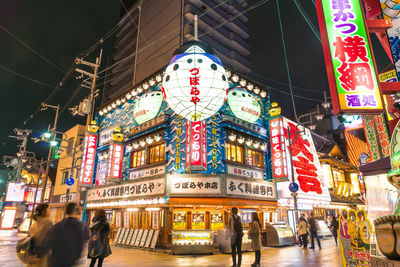 People on illuminated street amidst buildings in city at night