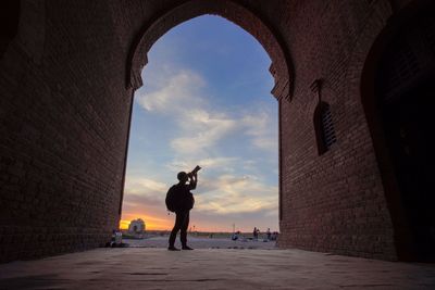 Silhouette man photographing historic building against sky during sunset