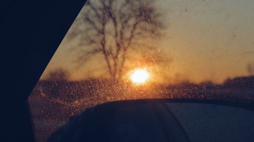 Close-up of wet car windshield against sky during sunset