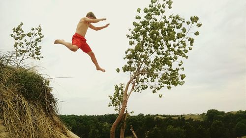 Low angle view of woman jumping against clear sky