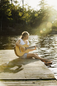 Young woman on jetty playing guitar
