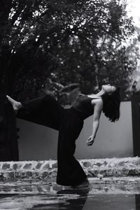 Full length of woman standing on one leg against tree