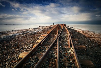 Railroad tracks amidst field against cloudy sky during winter