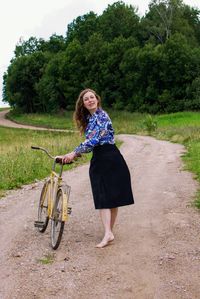 Full length portrait of young woman with bicycle on road