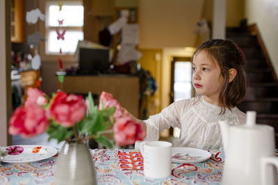 A small child in a lace dress sits alone at a table set for tea party