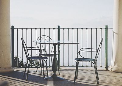 Chairs on railing by sea against sky