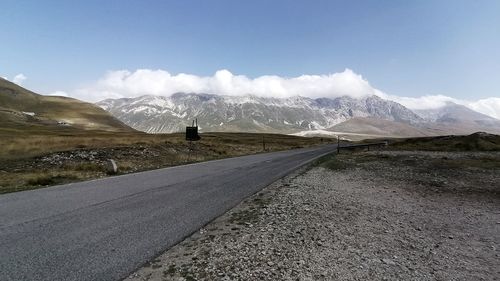 Empty road leading towards mountains against sky