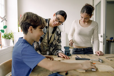 Smiling young teacher with male and female students during carpentry class