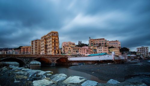 Arch bridge over river amidst buildings in city against sky