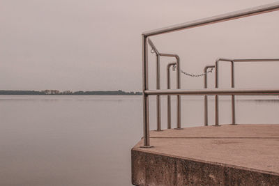 Metal railing by lake against sky