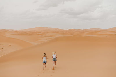 People on sand dune in desert against sky