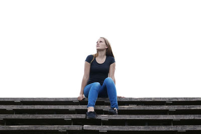 Low angle view of thoughtful young woman sitting against clear sky