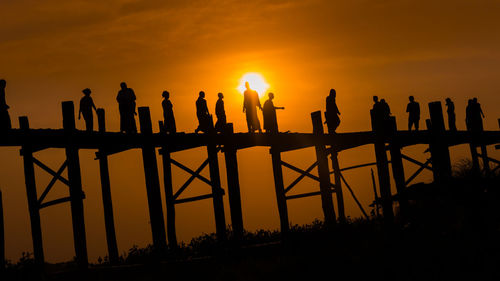 Silhouette people walking on bridge against sky during sunset