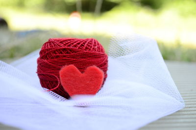 Close-up of heart shape by red thread spool on white tulle netting