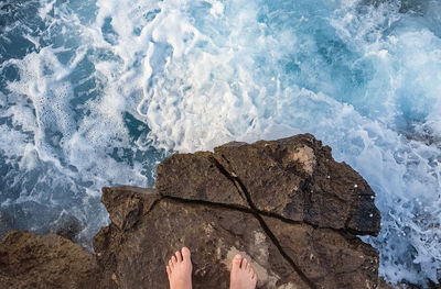 Personal perspective of man standing on rock by sea. splashing water, waves.