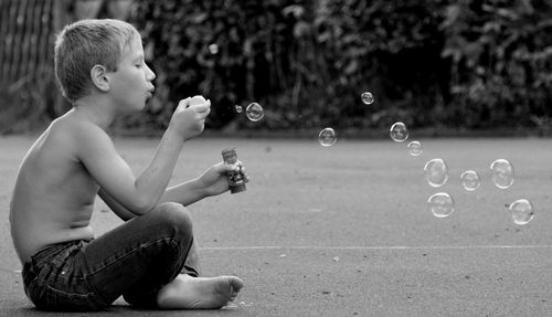 Shirtless boy blowing bubbles on road