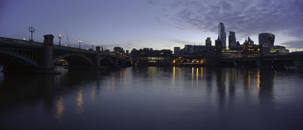 Illuminated bridge over river against sky in city at dusk