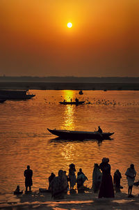 Silhouette people in sea against sky during sunset