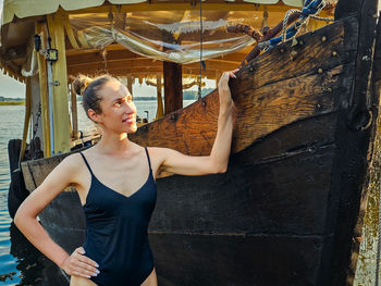 Slim sticky woman in a swimsuit near an old wooden boat in the rays of sunlight