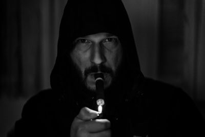 Portrait of man wearing hooded shirt lighting cigar at home