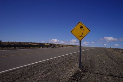 Road sign on country road against blue sky