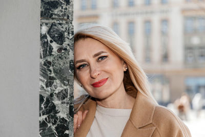 Woman in beige attire leaning on marble wall, city background