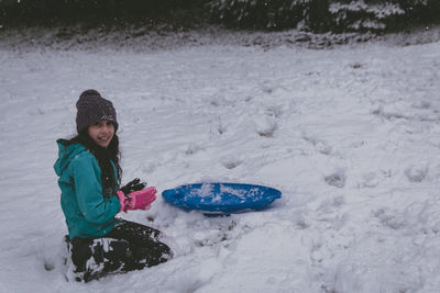 Full length of girls sitting on bobsled in snow