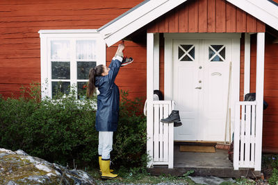 Side view of young woman drying shoes outside house