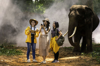 Full length of man holding elephant standing against waterfall