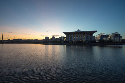 Illuminated building by lake against blue sky at dusk