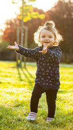Smiling cute baby girl standing in park at sunset