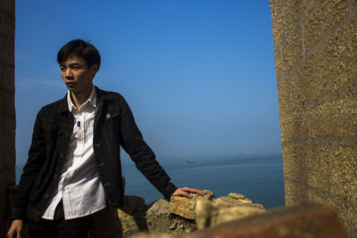 Man standing on rock by sea against clear sky