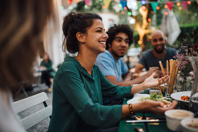 Smiling young women gesturing while sitting with friends at table during dinner party