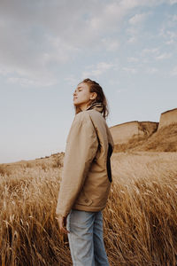 Side view of young woman standing on field against sky