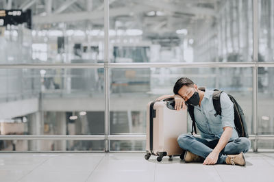 Full length of man sitting by suitcase at railroad station