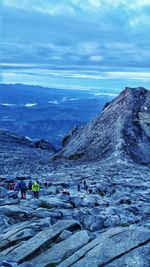 People on rocks by mountain against sky