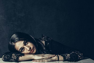 Portrait of young woman lying down against black background