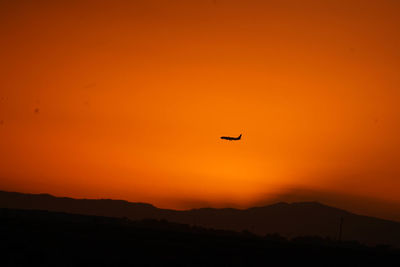 Silhouette of a plane flying in orange sky