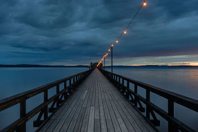 Long wooden pier over a river at night with lights strung overhead