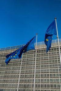 Low angle view of flags on building against blue sky