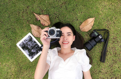 Portrait of smiling young woman photographing with camera while lying on grassy land