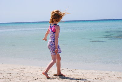 Rear view of girl walking on shore against sea and sky