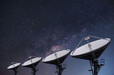 Low angle view of satellite dishes against star field sky at night