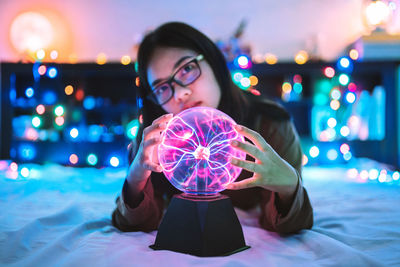 Portrait of woman holding plasma ball on bed