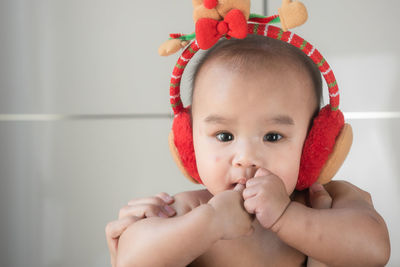 Cropped image of hands holding cute baby boy wearing ear muff against wall