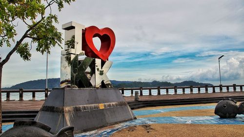 Red heart shape by boat on river against sky