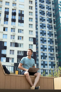 Full length of man sitting against modern building in city