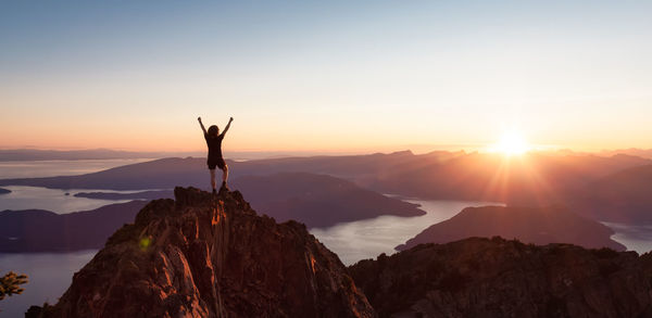 Silhouette person standing on rock against sky during sunset