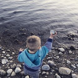 Rear view of boy holding pebble while standing at beach