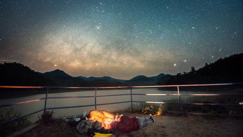 Couple lying by bonfire at lakeshore against sky